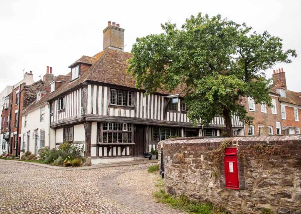 Half timbered house in Rye sits behind the stone wall of the graveyard which has a red post box built into it