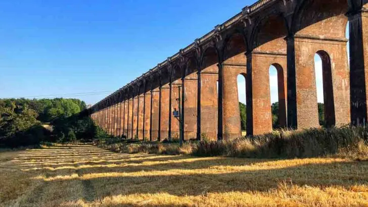 Ouse Valley Viaduct near Balcombe, West Sussex. The red brick arches of this viaduct cast shadows across the recently mown field to the left and the setting sun shines through the pillars
