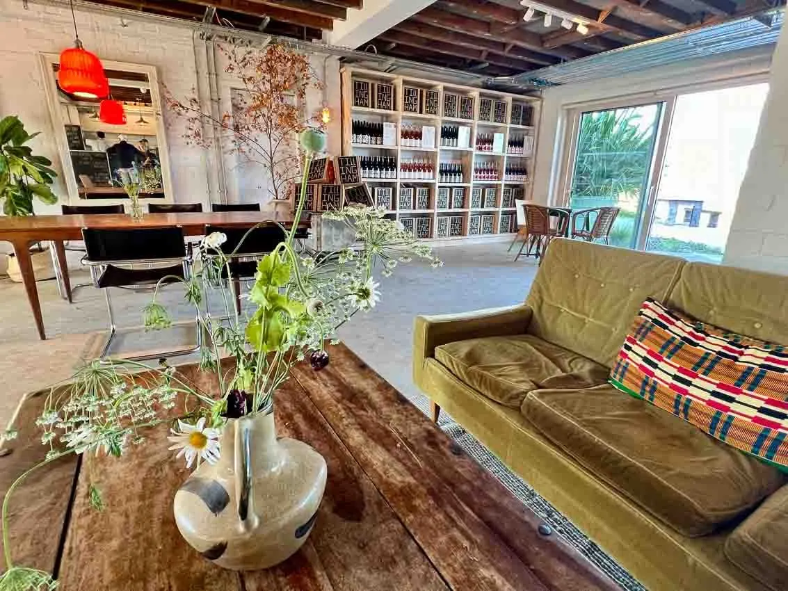 Mid century olive green sofa with orange cushion and wild flowers in a jug on a coffee table