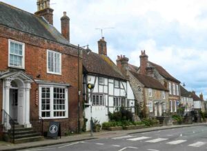 Steyning High Street in West Sussex. Different styles and ages of building looking down the left hand side of the street from flint and half-timbered cottages to a Georgian house with pillared porticoe. A zebra crossing can be seen on the road