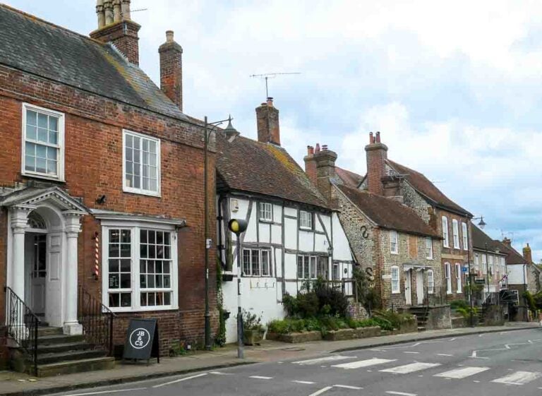 Steyning High Street in West Sussex. Different styles and ages of building looking down the left hand side of the street from flint and half-timbered cottages to a Georgian house with pillared porticoe. A zebra crossing can be seen on the road