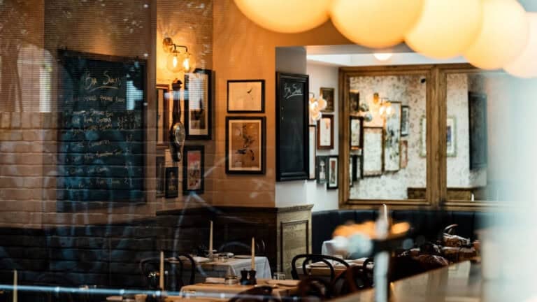 Crazy Goose, Brighton. Looking through a window into a warm cozy bar and restaurant with candles on tables and pictures on the walls. A blackboard on the wall has the bar snacks chalked up