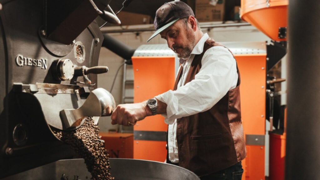 Man in a cap and waistcoat roasting cofee beans. Edge tea and coffee